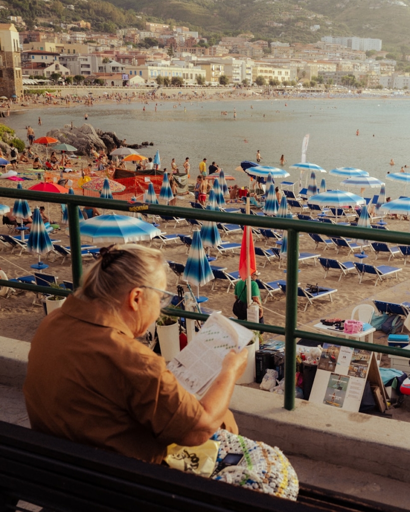 Woman reading on a bench overlooking a crowded beach.