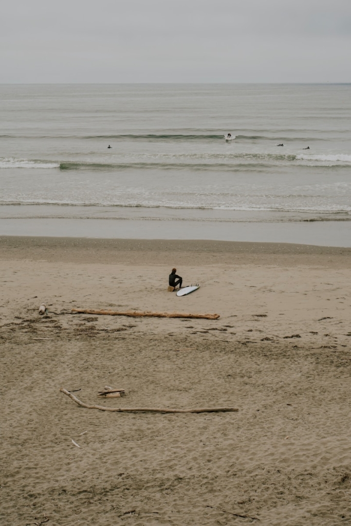 Surfer sits on beach with surfboard near ocean waves